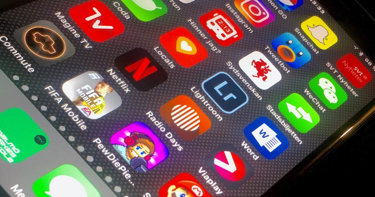 En närbild av en smartphone-skärm som visar olika färgglada appikoner, inklusive Netflix, Word, Snapchat, Lightroom och flera spel, mot en mörk, prickig bakgrund.