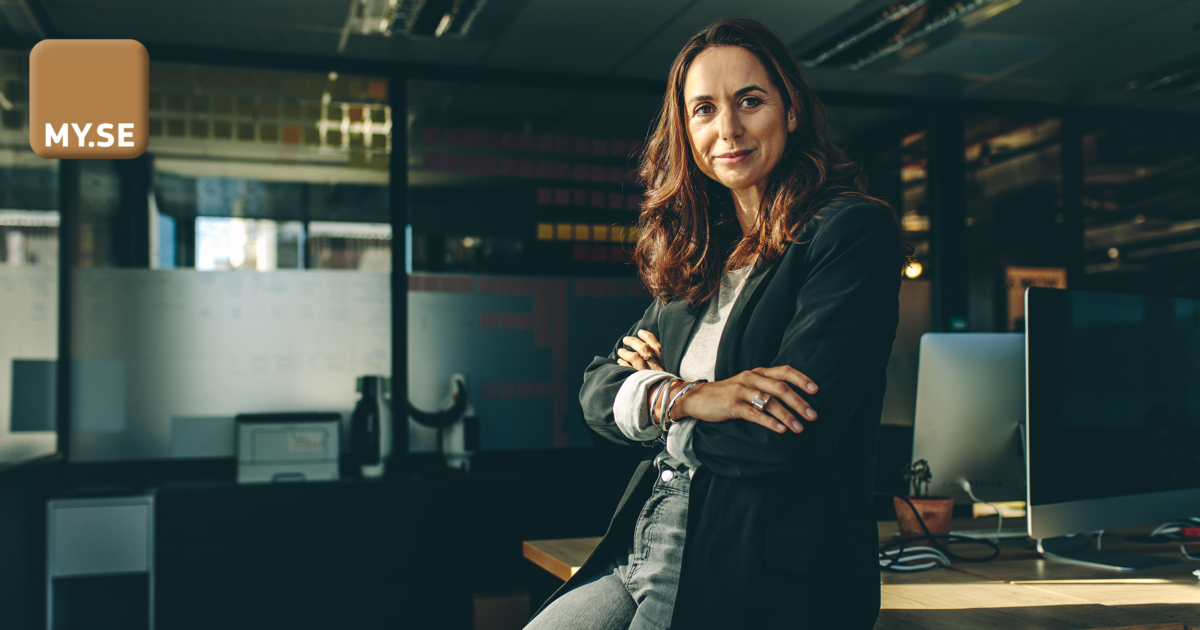 En självsäker kvinna med långt brunt hår, iklädd svart kavaj och grå skjorta, står med armarna i kors i ett modernt kontor. En MY.SE-logotyp syns i bildens övre vänstra hörn.