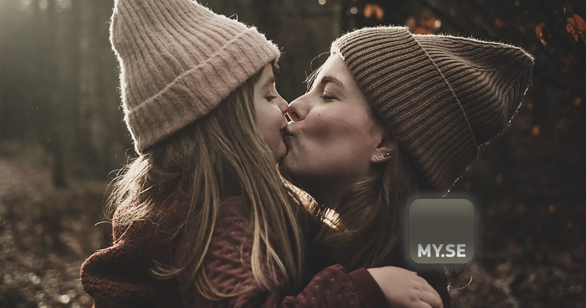 En kvinna och en ung flicka i stickade mössor delar en kärleksfull kyss utomhus i en skog. Kvinnan håller barnet, och de är båda varmt inlindade. Bilden har en MY.SE-logotyp i det nedre högra hörnet.
