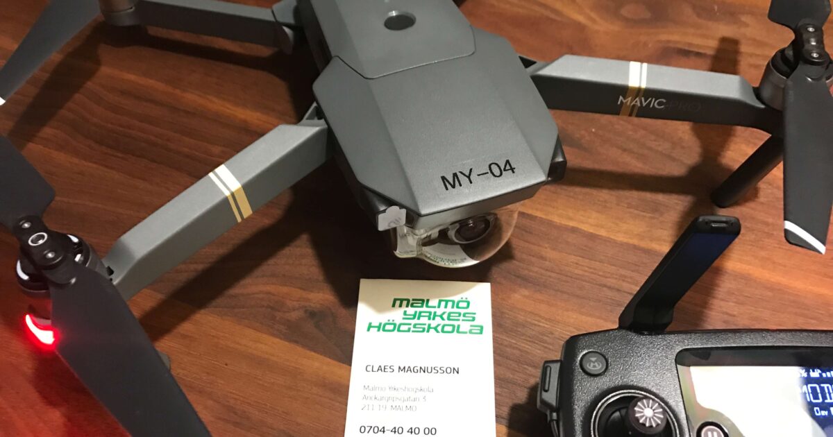 En grå drönare märkt MY-04, en fjärrkontroll och ett visitkort från Malmö högskola placeras på en träyta. Visitkortet visar kontaktinformation till Claes Magnusson.