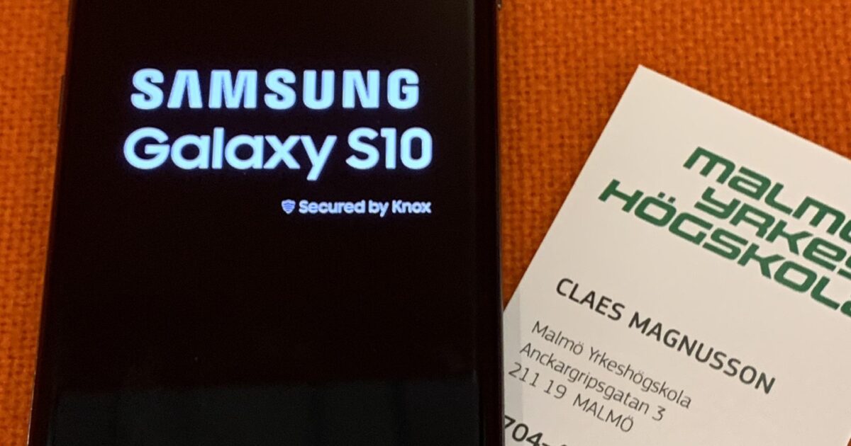 En Samsung Galaxy S10 smartphone visar sin startskärm bredvid ett Malmö Yrkeshögskola visitkort för Claes Magnusson, vilande på en orange yta.