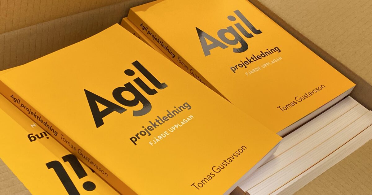 En låda fylld med flera exemplar av en gul bok med titeln Agil projektledning av Tomas Gustavsson, med några böcker liggande och andra stående.