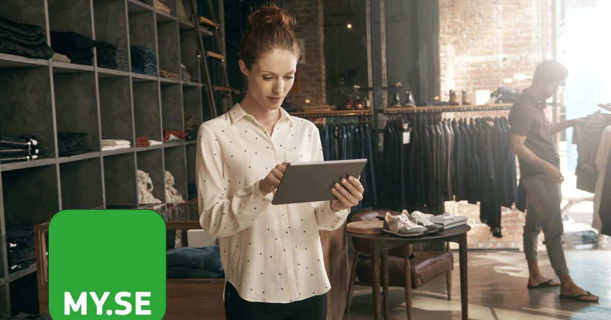 En kvinna står i en klädaffär och använder en surfplatta. Klädställ fyller bakgrunden. En person handlar i närheten. En grön fyrkant med MY.SE visas i det nedre vänstra hörnet. Solljus strömmar in genom stora fönster.