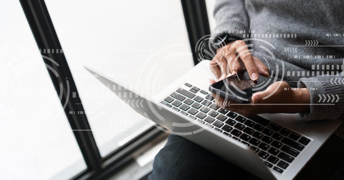 En person som sitter vid ett fönster och använder en smartphone och en bärbar dator, med digital nätverksgrafik över bilden, vilket antyder teknologi eller kommunikation.