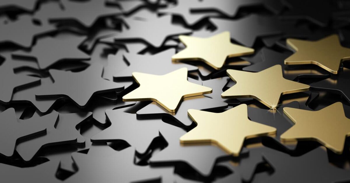 En grupp glänsande guldstjärnor sticker ut bland ett spritt lager av mattsvarta stjärnor på en reflekterande mörk yta.