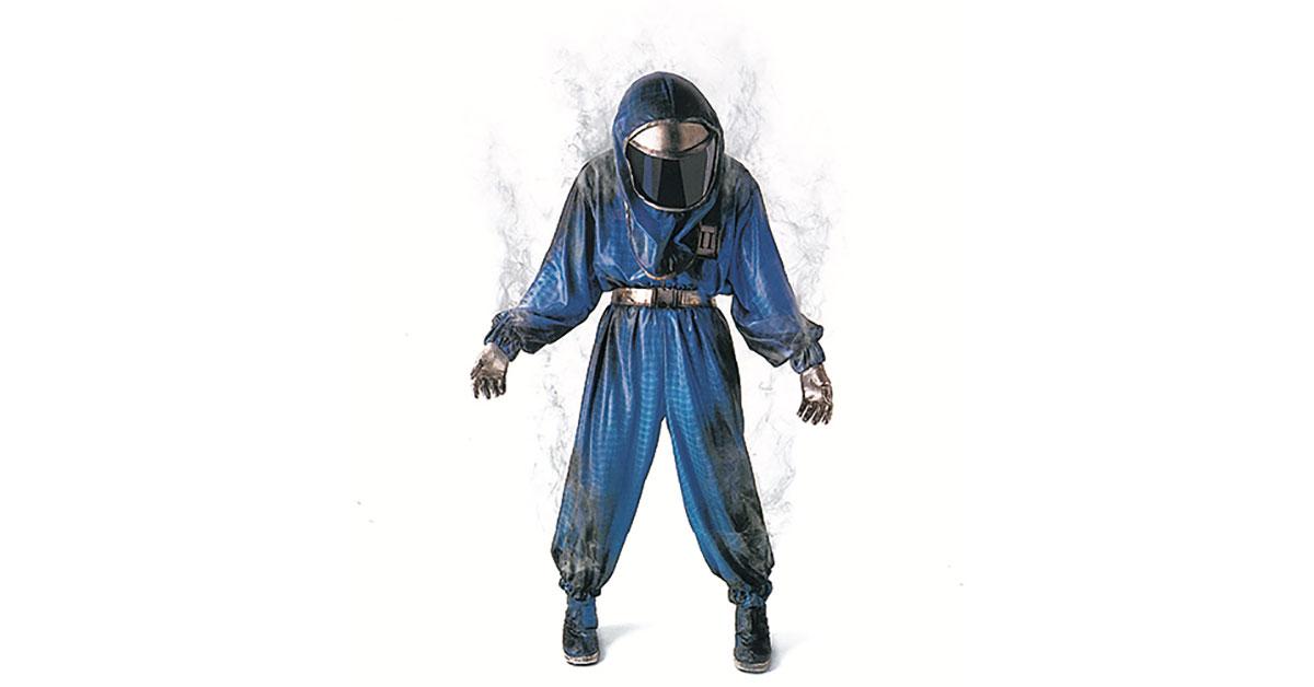 En person står vänd framåt och bär en helkroppsskyddande blå skyddsdräkt med hjälm och ansiktsskydd, handskar och täckta skor. Dräkten verkar avge en svag dimma eller ånga runt kanterna.