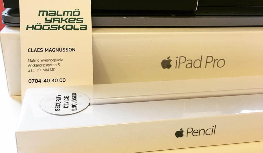 Ett visitkort från Malmö Yrkeshögskola vilar på staplade Apple-produktkartonger för en iPad Pro och Apple Pencil, med en säkerhetsklistermärke i närheten och en del av ett annat paket synlig i bakgrunden.