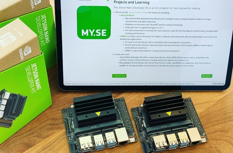 Två NVIDIA Jetson Nano-utvecklarpaket placeras på en träyta framför en öppen bärbar dator som visar en webbsida om projekt och utbildning. Två Jetson Nano-lådor är staplade på vänster sida.