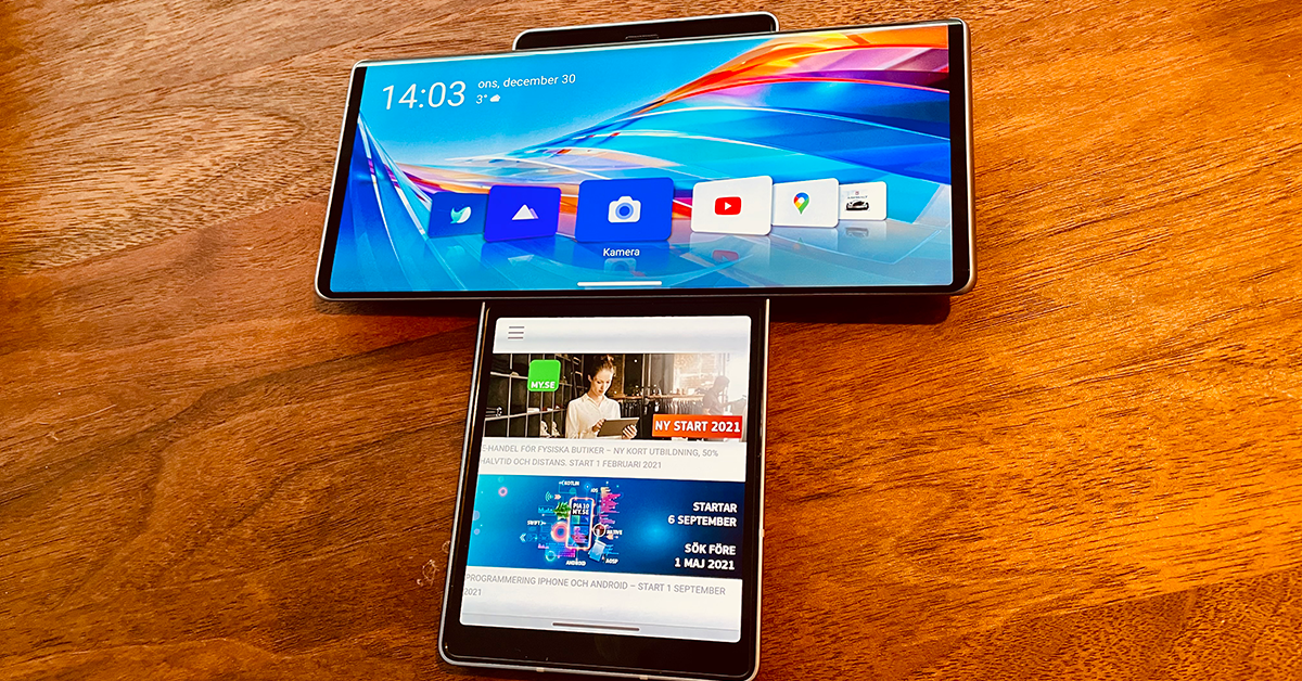 Två smartphones är placerade i ett T-format på en träyta. Den övre telefonen visar en färgglad startskärm, medan den nedre telefonen visar en webbplats med artiklar och bilder.