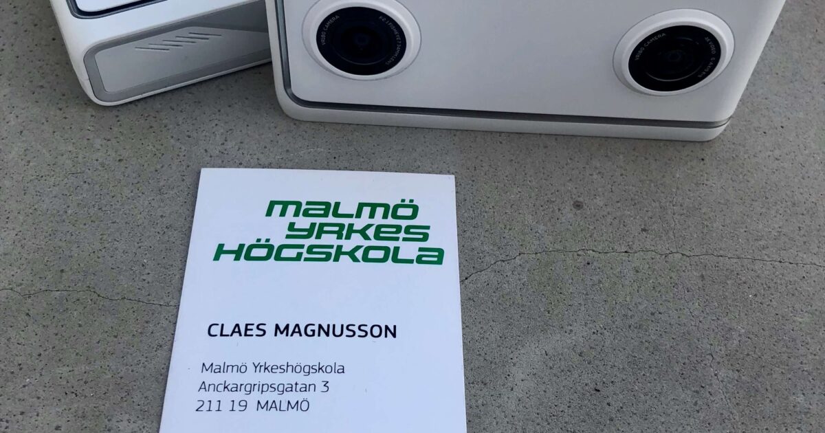 Två vita 3D-kameror är placerade på en grå yta bredvid ett visitkort för Claes Magnusson, Malmö Yrkeshögskola, med kontaktuppgifter inklusive telefonnummer, e-postadress och länkar till sociala medier.