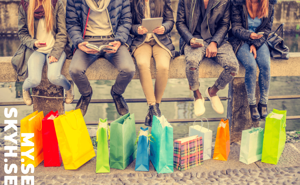 Sex personer sitter på en stenhylla med färgglada shoppingkassar vid fötterna. De bär vardagsjackor och jeans, och några håller i telefoner eller böcker. Bilden har texten "MY:SE SKYH.SE" på vänster sida.