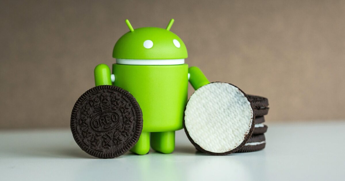 En grön Android-robotfigur står mellan en hög med Oreo-kakor och två kakor, en hel och en delad för att visa krämfyllningen, mot en slät bakgrund.