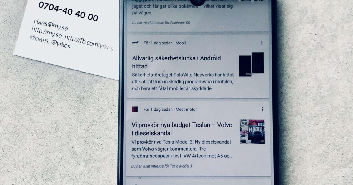Ett visitkort för Claes Magnusson från Malmö Yrkeshögskola ligger på en yta bredvid en smartphone som visar ett nyhetsflöde med artiklar på svenska.