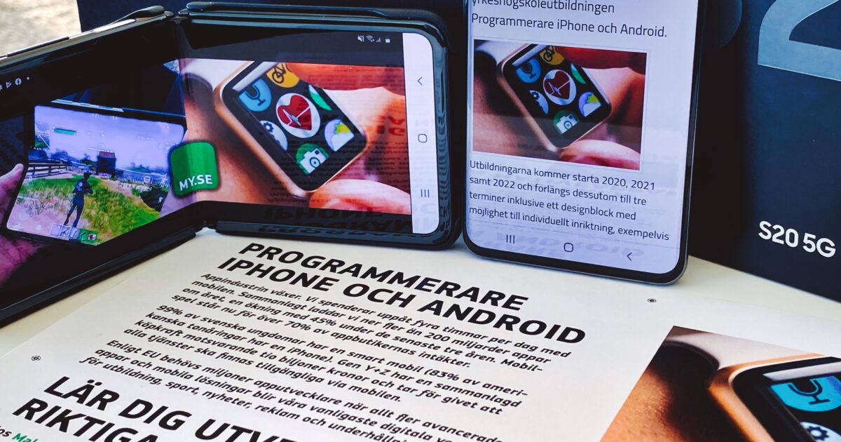 Två smartphones visar en programmeringsapp och en artikel, båda placerade på ett bord med tryckta broschyrer om att lära sig utveckla native-appar för iPhone och Android. En Samsung S20 5G-box syns delvis i bakgrunden.
