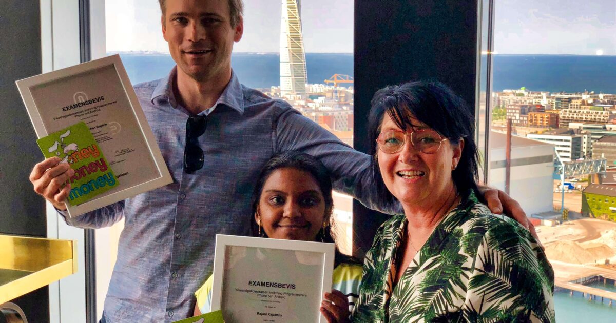 Tre personer ler och håller inramade certifikat framför ett stort fönster med utsikt över staden och havet. En person står och två sitter, med Turning Torso skyskrapa synlig i bakgrunden.