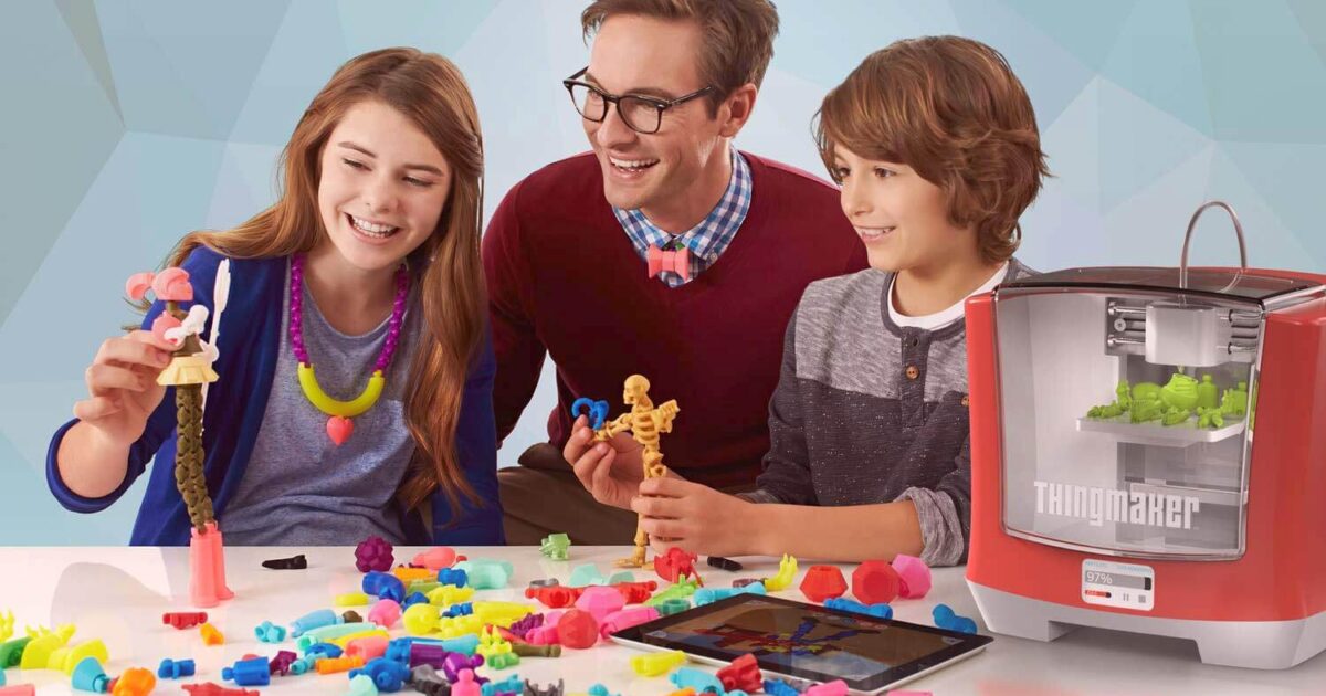 Tre leende barn leker med färgglada 3D-utskrivna leksaker vid ett bord, med en röd ThingMaker 3D-skrivare och en surfplatta i närheten, omgivna av olika färgglada plastskapelser.