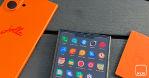 En Jolla-smartphone med det orange bakstycket borttaget, där startskärmen med färgglada appikoner syns. Två orange bakstycken ligger dessutom bredvid på en mörk träyta.