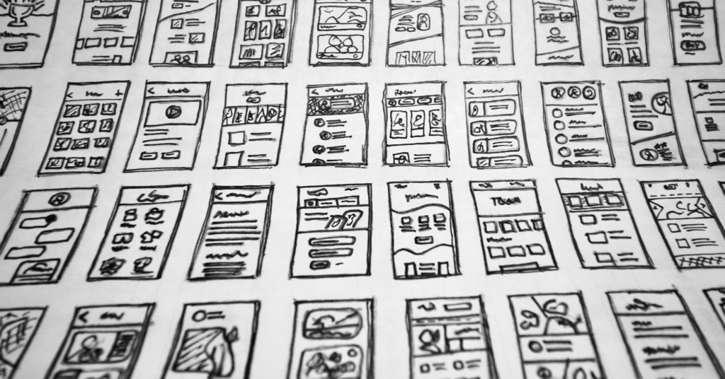 uxvt27 Svartvitt foto som visar flera handritade wireframes för mobilappar eller webbplatser, ordnade i prydliga rader på papper. Varje wireframe innehåller olika layouter med rutor och ikoner som illustrerar olika koncept för användargränssnittsdesign.